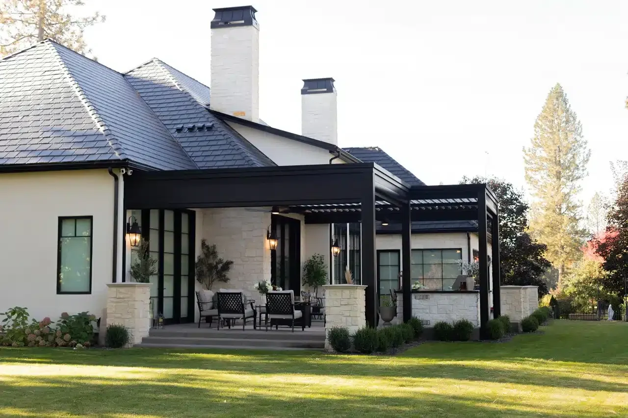 Black Azenco R-BLADE™ louvered pergola attached to a stone patio at a white home
