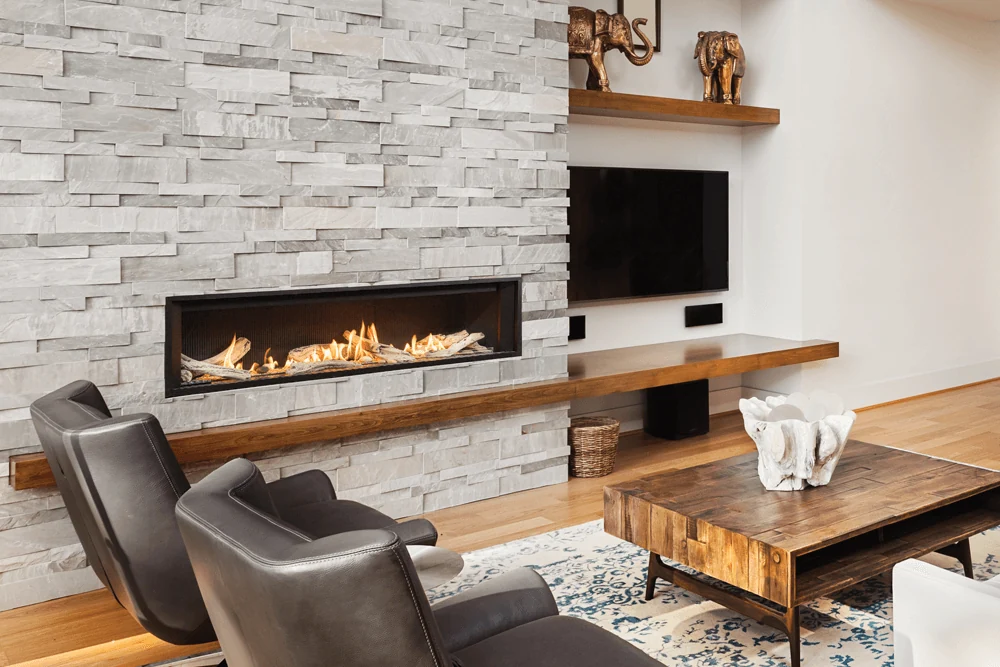 Valor L3 linear gas fireplace with driftwood and fluted black liner in a stone feature wall